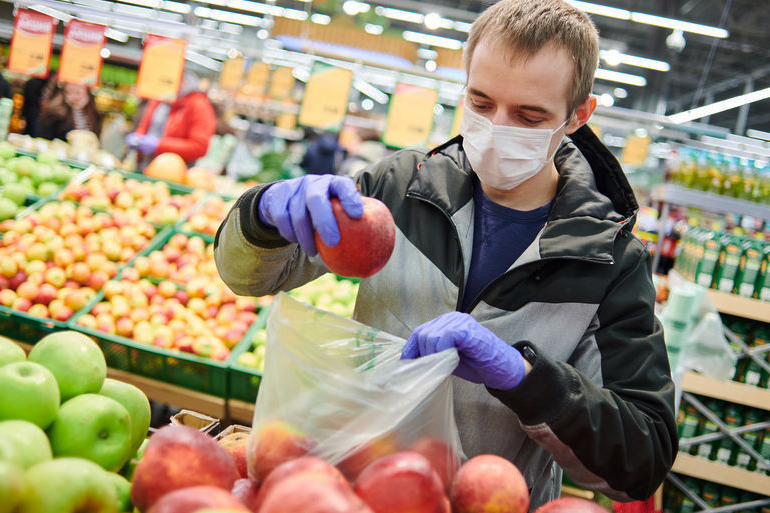 Man wearing surgical mask and looking at fruit at grocery store during coronavirus pandemic