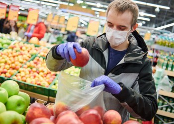 Man wearing surgical mask and looking at fruit at grocery store during coronavirus pandemic