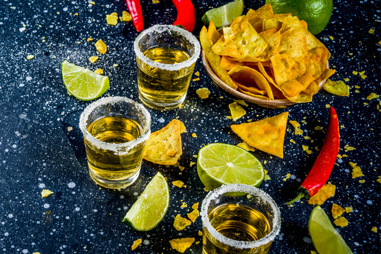 Cinco de Mayo celebration concept. 5th May Mexican party's drinks - margarita cocktail, tequila shots with lime, hot chili peppers and chips, dark background copy space