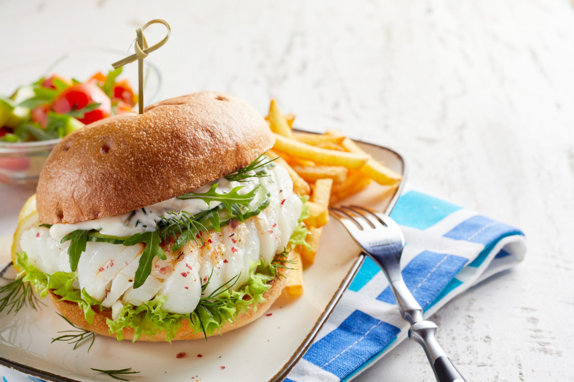 Spicy fish burger with fresh rocket and mayonnaise on a crusty toasted bun served with French fries and salad