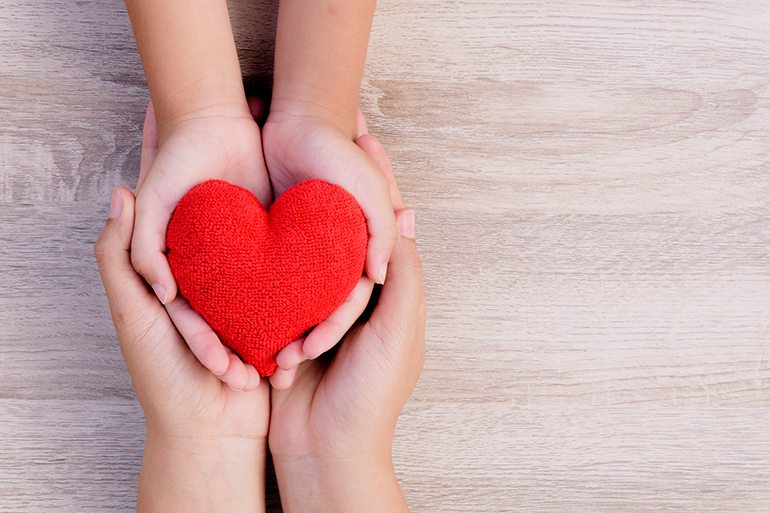 Health care, love, organ donation, family insurance and CSR concept. adult and child hands holding handmade red heart on wooden background.