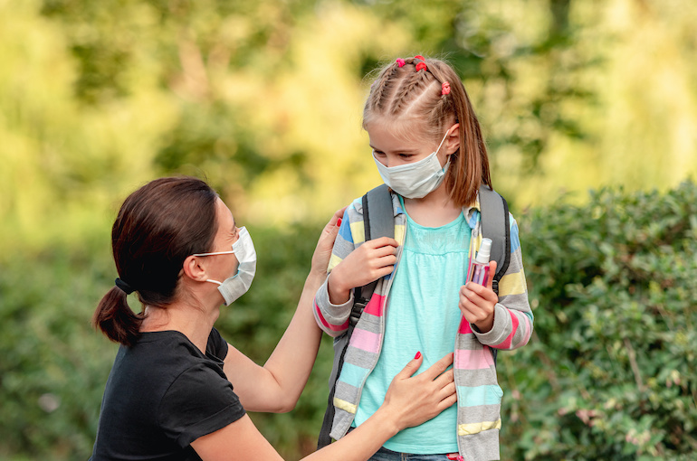 Mother putting mask on daughter before school