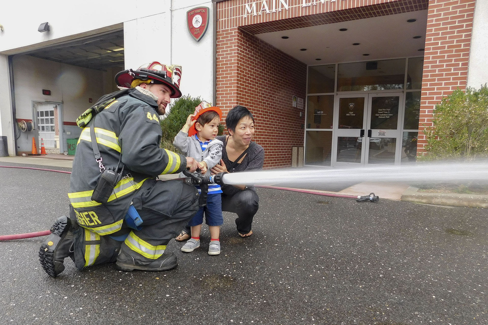 Young Finn Frazer tries his hand at using a hose with the help of mom and East Hampton Firefighter Sam Fisher during the East Hampton Fire Department Open House on Sunday, October 7th, 2018