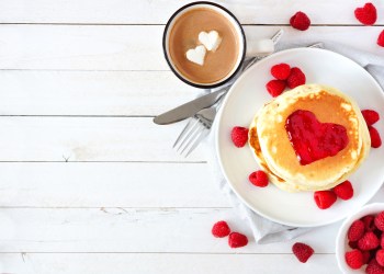 Love concept breakfast with pancakes, hot chocolate and raspberries over white wood
