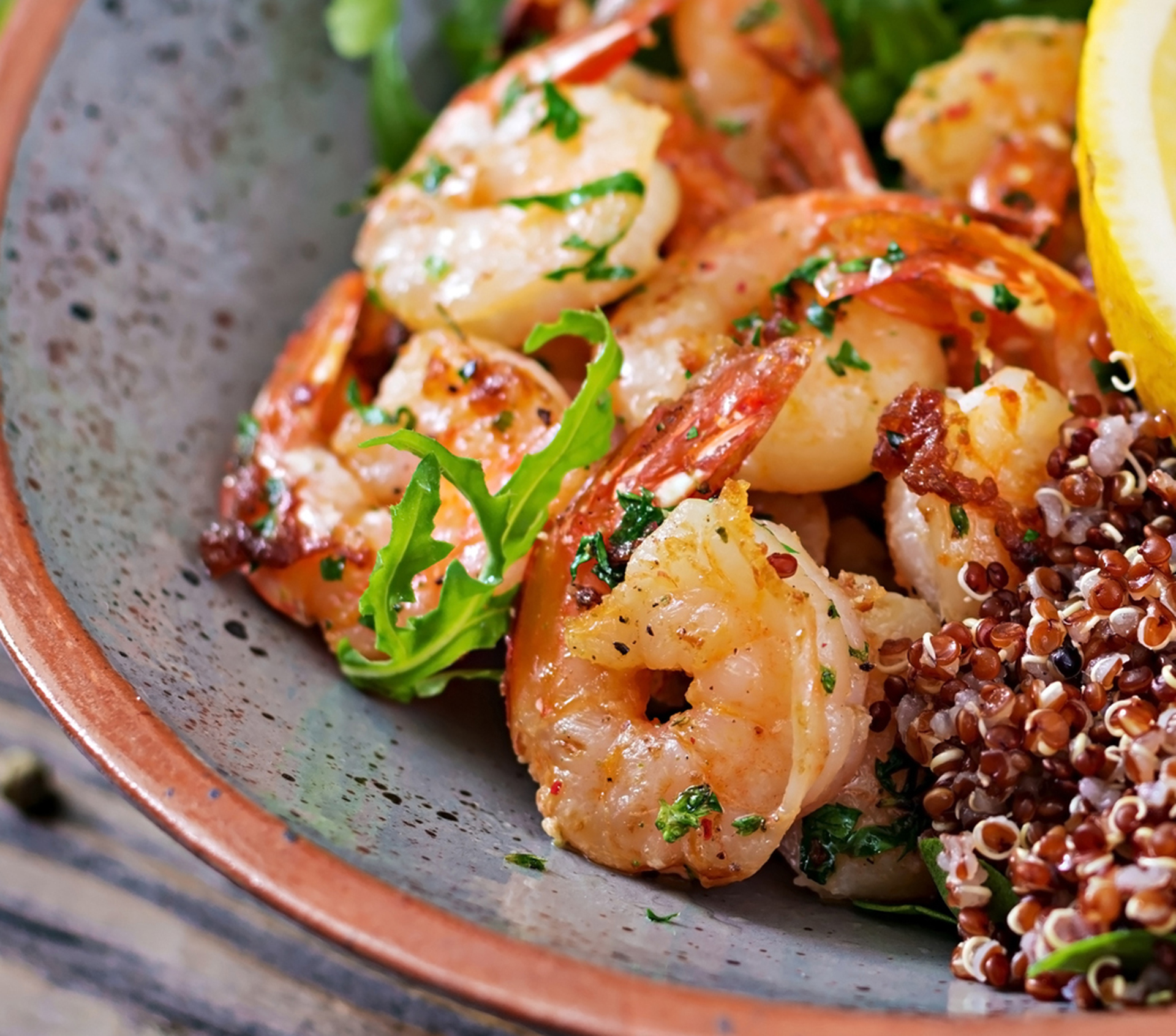 Delicious healthy Buddha bowl with shrimps, tomato, avocado, quinoa, lemon and arugula on the wooden table. Healthy food.