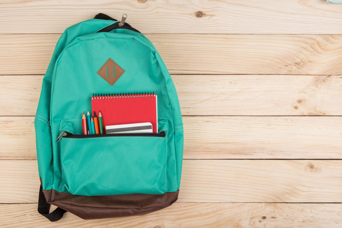 blue backpack, red notebooks and pencils on wooden table