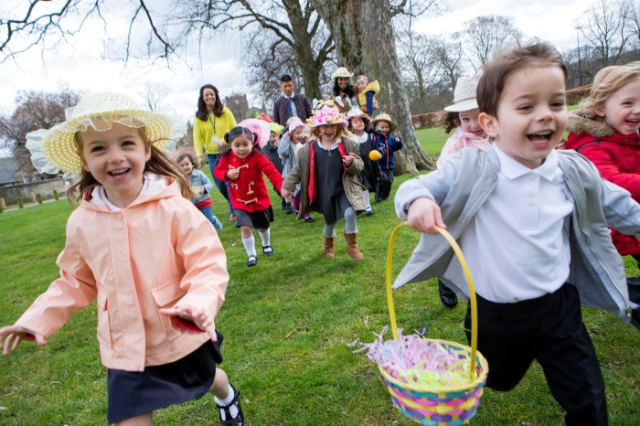 Nursery children running across a field during their outdoor Easter egg hunt, they are wearing handmade hats and carrying baskets.