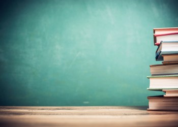 Textbooks on wooden school desk with chalkboard.