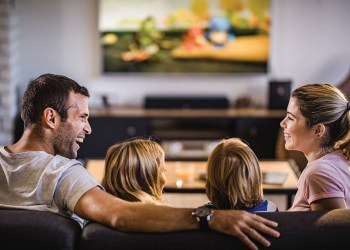Happy parents talking while watching TV with their kids at home.