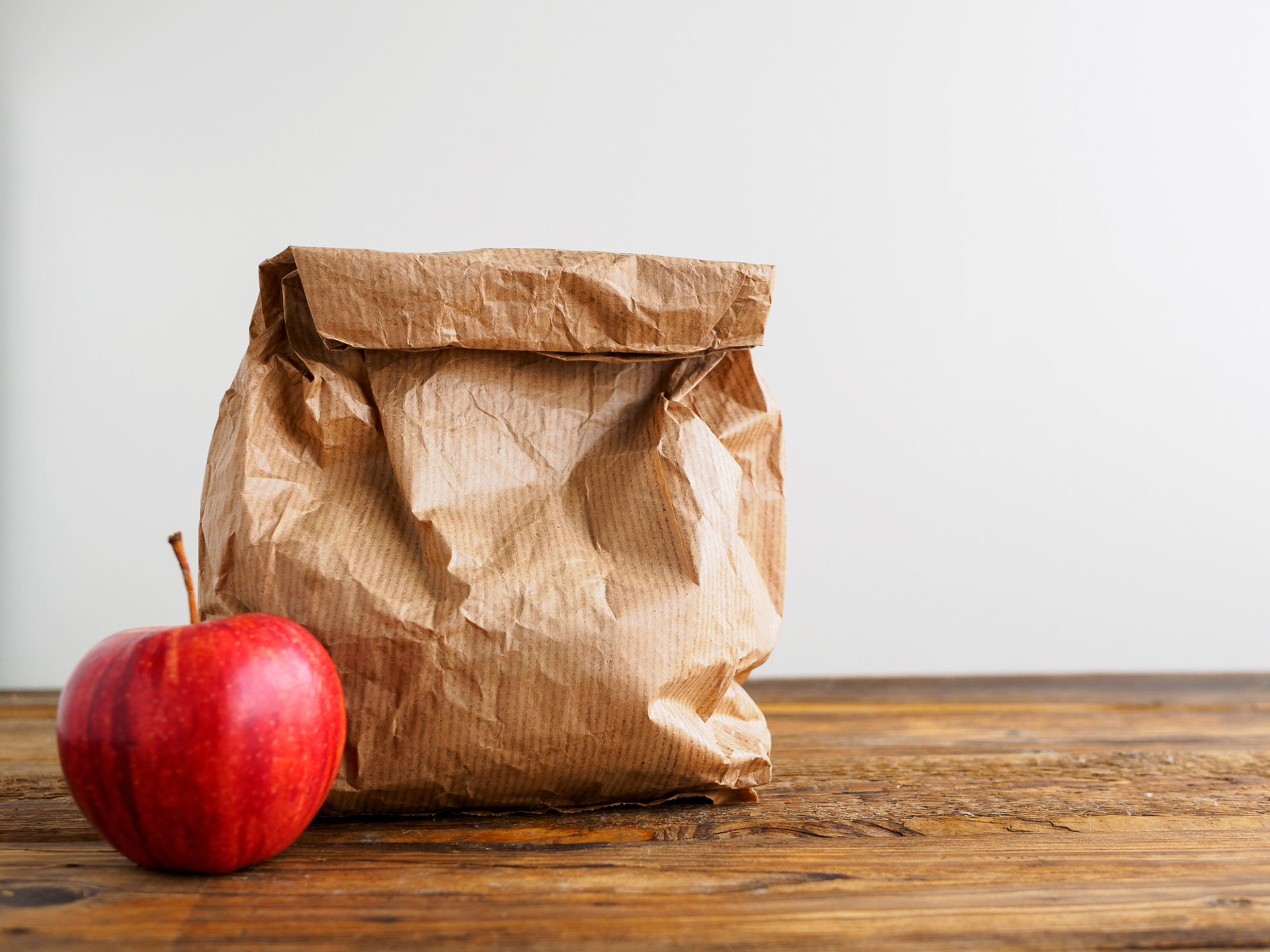 Papiertüte mit Pausenbrot und ein roter Apfel