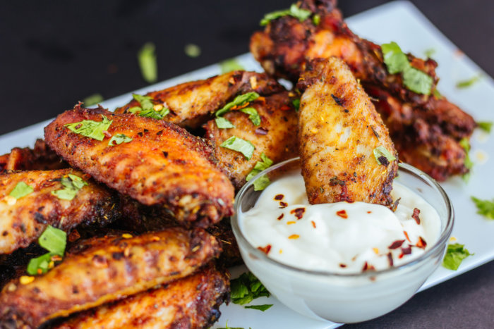 Spicy Chicken Wings with Cilantro, White Sauce and Chili Flakes on White Platter, Dark Background Photo