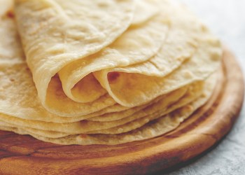 Stack of homemade wheat flour tortilla wraps on wooden cutting board.