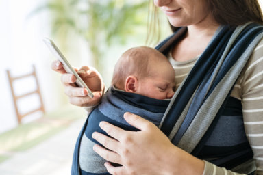 Unrecognizable mother with her son in sling and smartphone