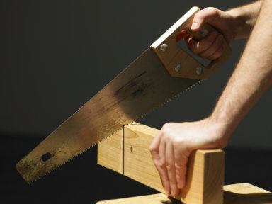 Man cutting through block of wood using saw, close-up of hands