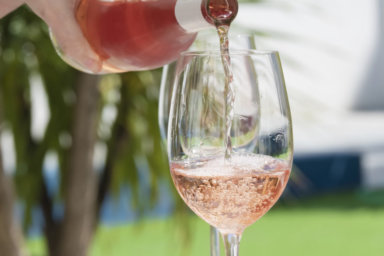 close up of a hand pouring delicious rose wine from bottle into glass outdoors . lifestyle concept