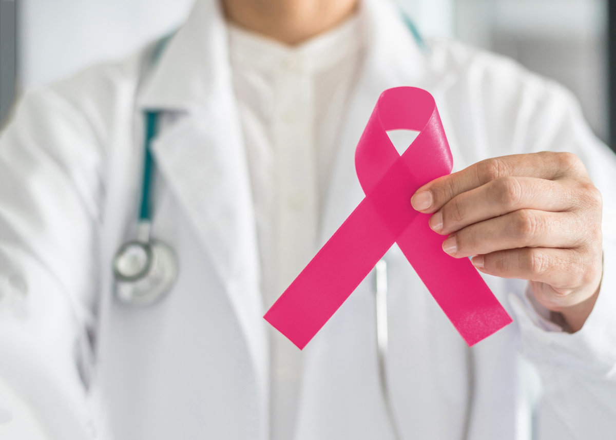 Pink ribbon for breast cancer awareness in doctor's hand, symbolic bow color for raising awareness campaign on women (female) patient living with breast tumor illness