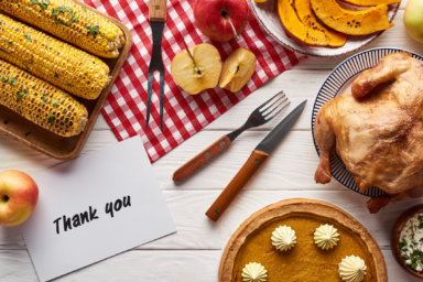 top view of pumpkin pie, turkey and vegetables served at white wooden table with thank you card for Thanksgiving dinner