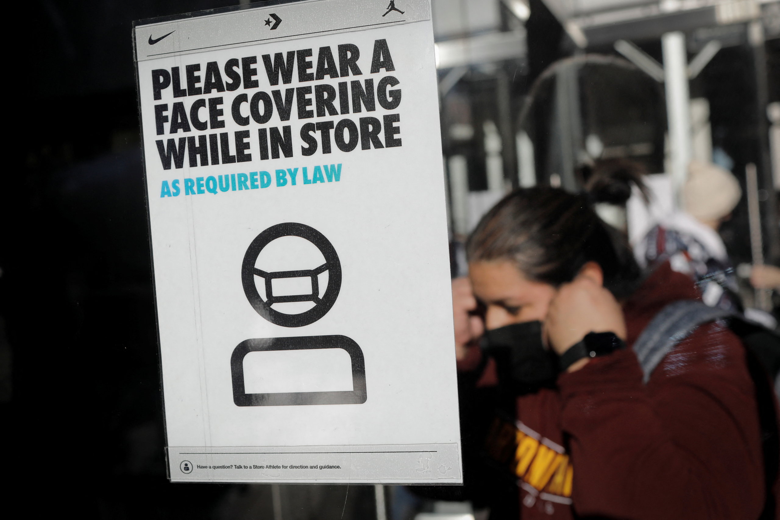 A shopper puts on a protective face mask as she enters a store, in accordance with the New York State indoor masking mandates that went into effect amid the spread of COVID-19