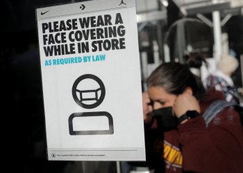 A shopper puts on a protective face mask as she enters a store, in accordance with the New York State indoor masking mandates that went into effect amid the spread of COVID-19