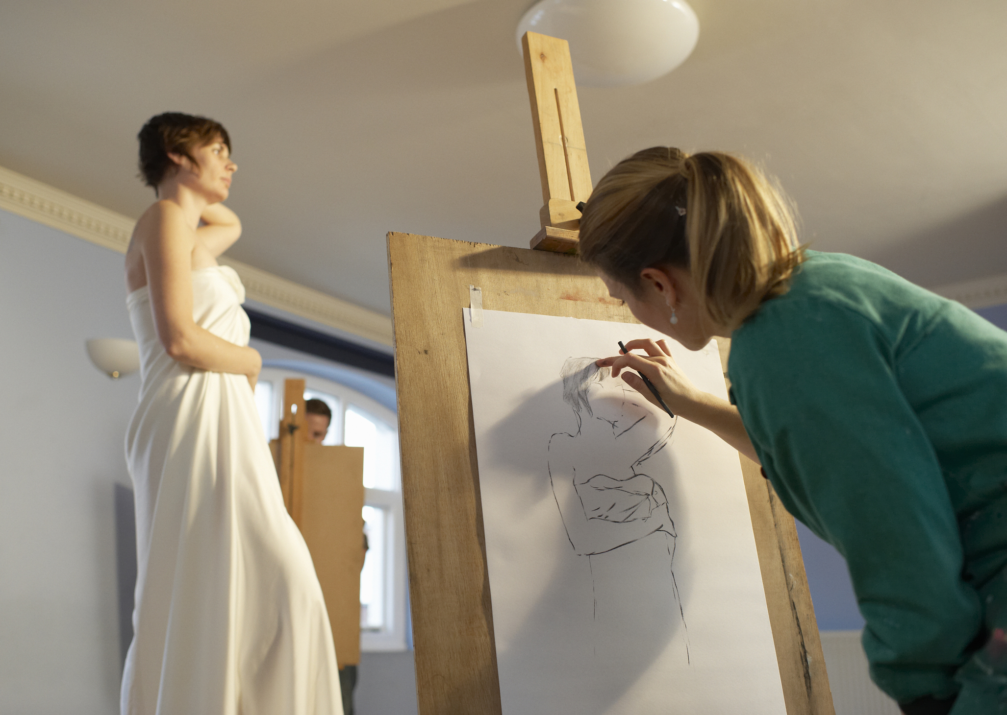 A woman at an easel working on a life-drawing.