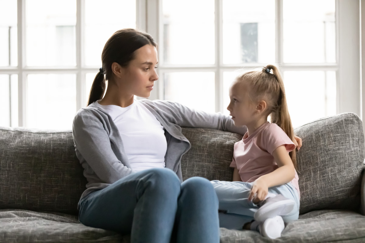 Serious young mom or nanny sit on couch with little preschooler girl talk sharing secrets, focused mother have conversation with small daughter, lecture or scold child, children upbringing concept