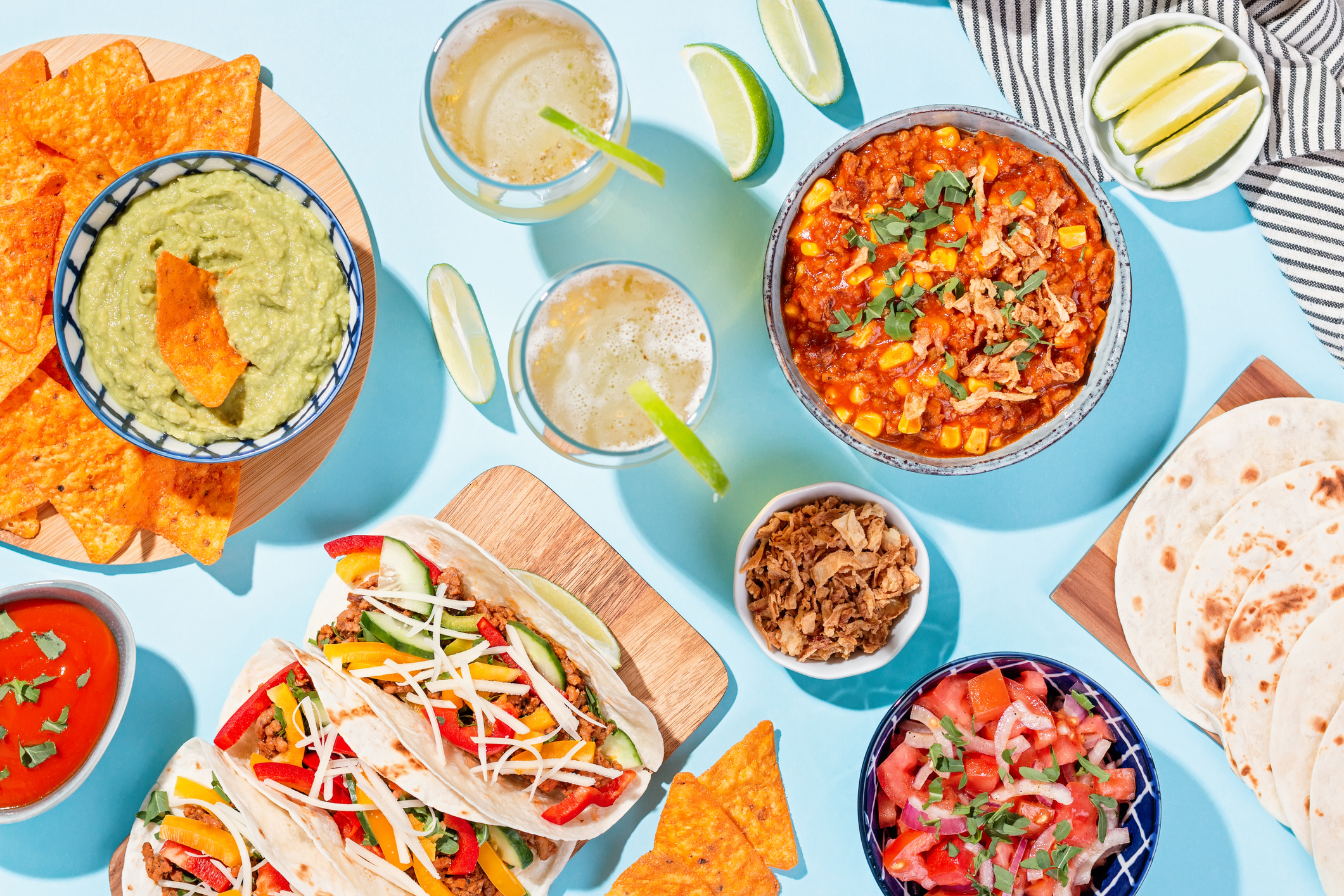 Mexican food table with traditional dishes. Chili con carne, tacos, tomato salsa, corn chips with guacamole Cinco de Mayo