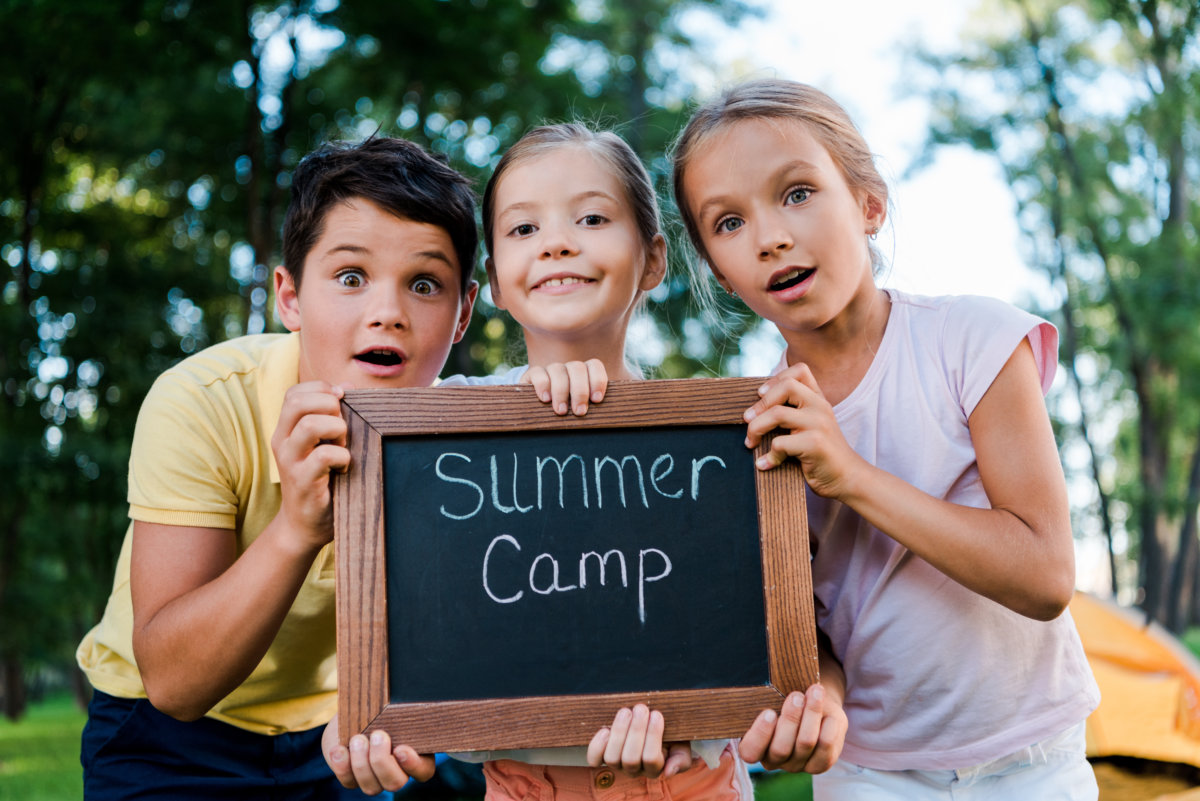 surprised kids holding chalk board with summer camp letters