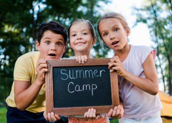 surprised kids holding chalk board with summer camp letters