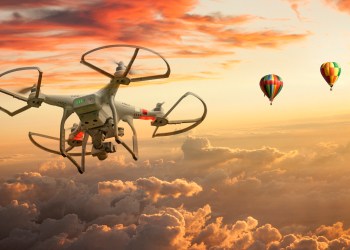 Two Hot air balloons and a drone floating over clouds at sunset