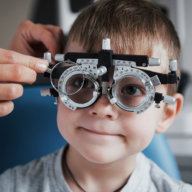 Tuning the intrument. Little boy with phoropter having testing his eyes in the doctor's office for back to school health checklist