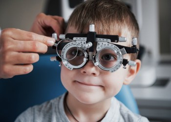 Tuning the intrument. Little boy with phoropter having testing his eyes in the doctor's office for back to school health checklist