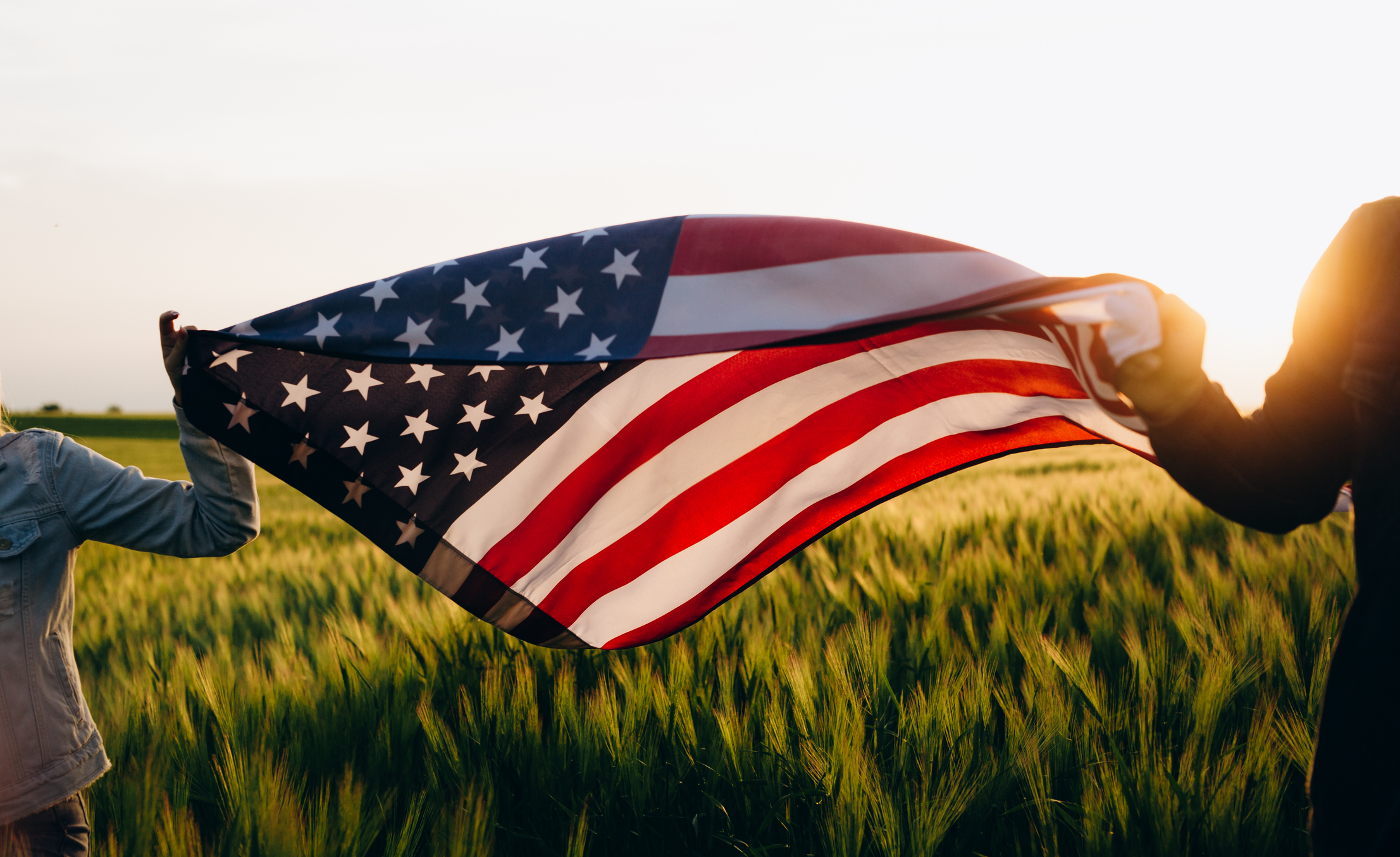 Hands holding American flag in a wheat field at sunset. Independence Day, 4th of July, American Independence