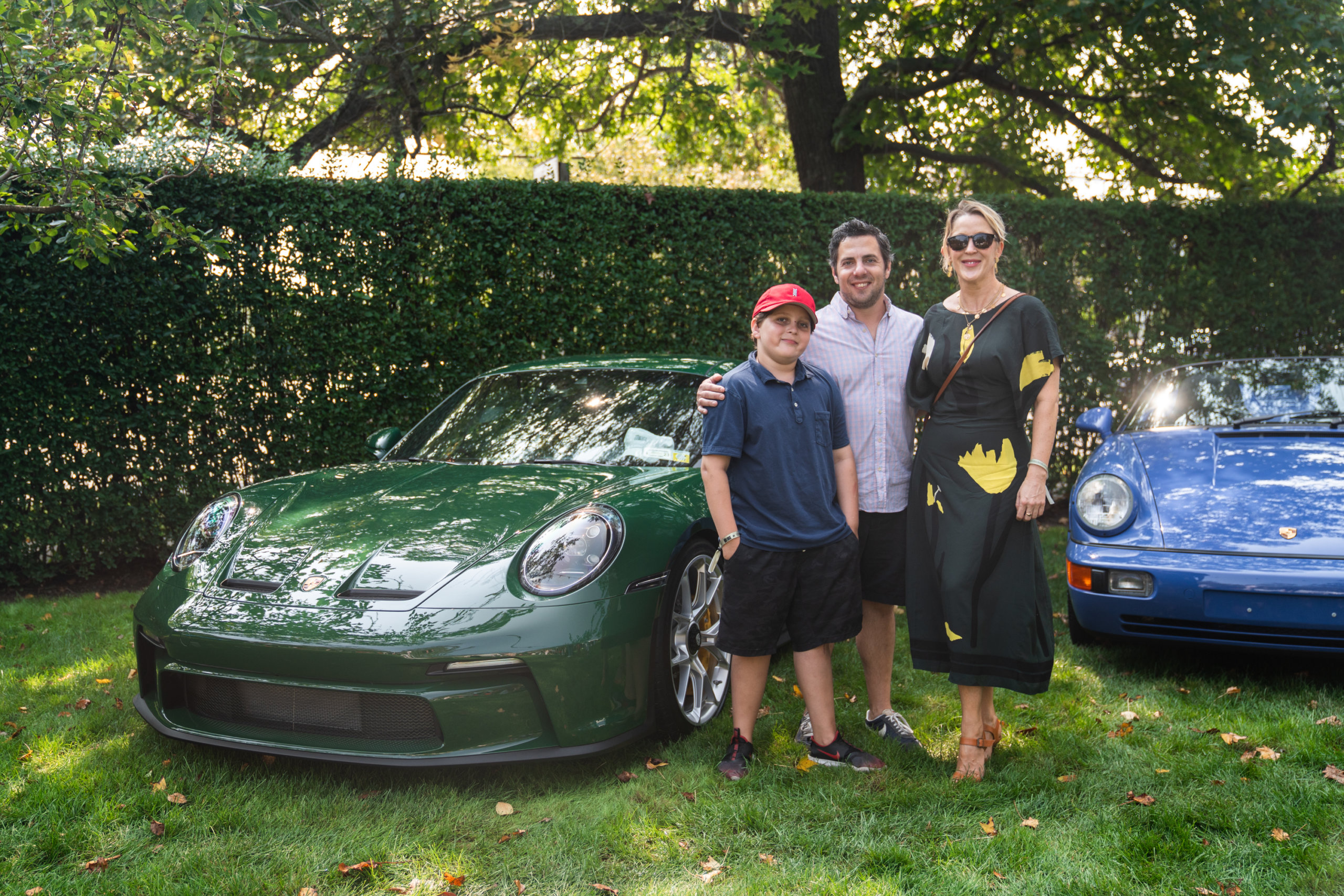 Greg and Lisa Strassberg with their son Senna posing in front of Jefferey Einhorn's "Irish Green" Porsche 911 GT3 Touring at Topping Rose House in Bridgehampton