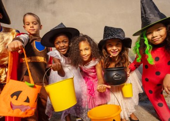 Many kids hold Halloween candy buckets and smile looking to the camera