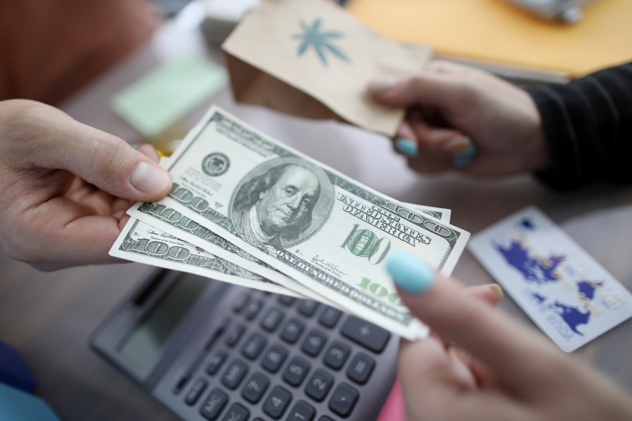 Close-up of persons hands giving money and taking package with ganja marihuana sign on it. Pack with cannabis sign on table. Sale of medical marijuana concept cannabis