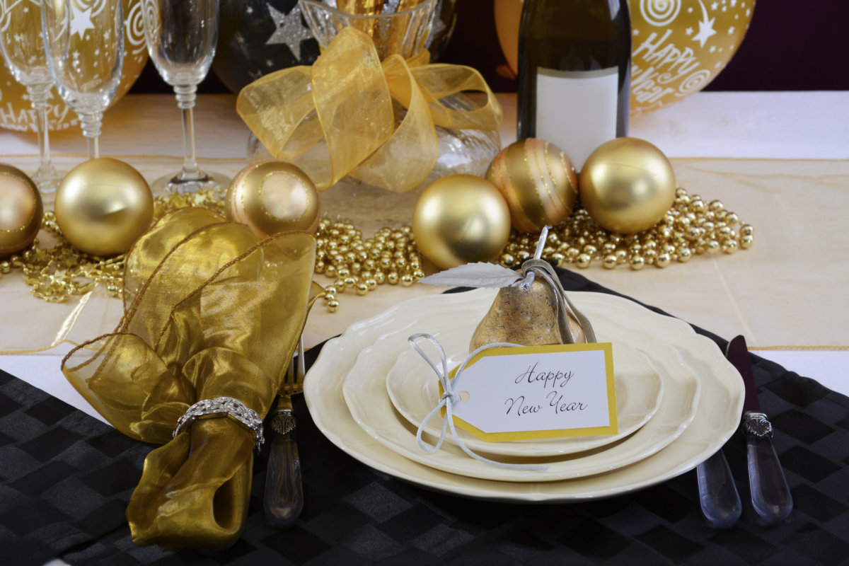 Happy New Year's Eve elegant dinner table setting with black and gold decorations, balloons and stylish centerpiece, close up.