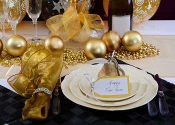 Happy New Year's Eve elegant dinner table setting with black and gold decorations, balloons and stylish centerpiece, close up.