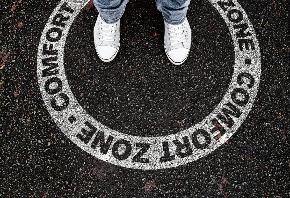 legs of person standing in circular marking on road with text COMFORT ZONE, being in or leaving own comfort zone concept