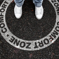 legs of person standing in circular marking on road with text COMFORT ZONE, being in or leaving own comfort zone concept