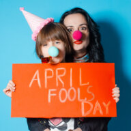Happy mother with her daughter holding a red sheet of paper with the inscription April Fool's Day. Spring day is a fool. The concept of a holiday and kids