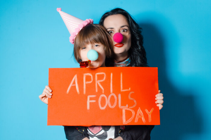 Happy mother with her daughter holding a red sheet of paper with the inscription April Fool's Day. Spring day is a fool. The concept of a holiday and kids