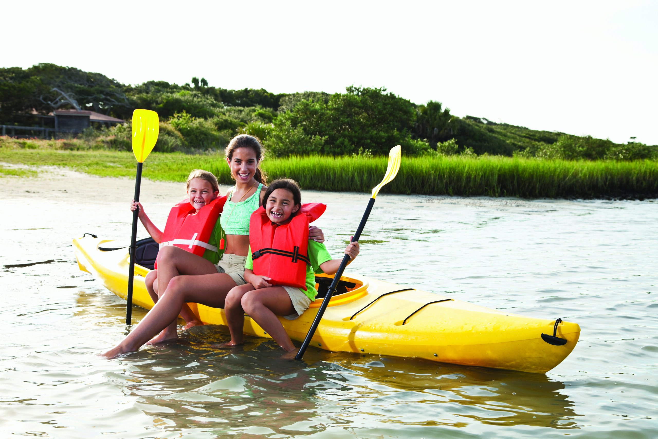 Teenage girl (17 years) with little girls (8-9 years) sitting on kayak in summer camp