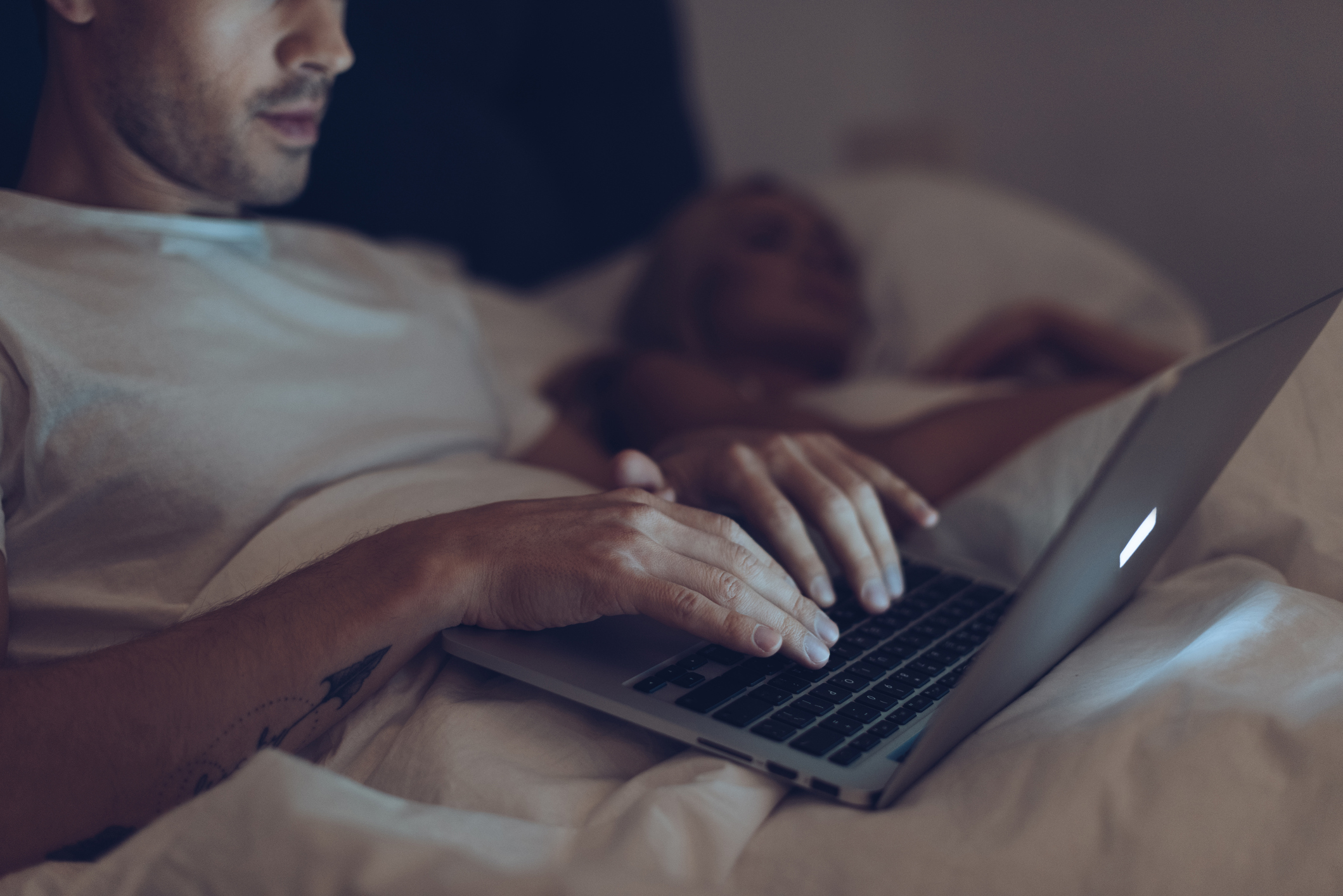 cropped shot of suspicious young man using laptop while wife sleeping in bed at night - no sex
