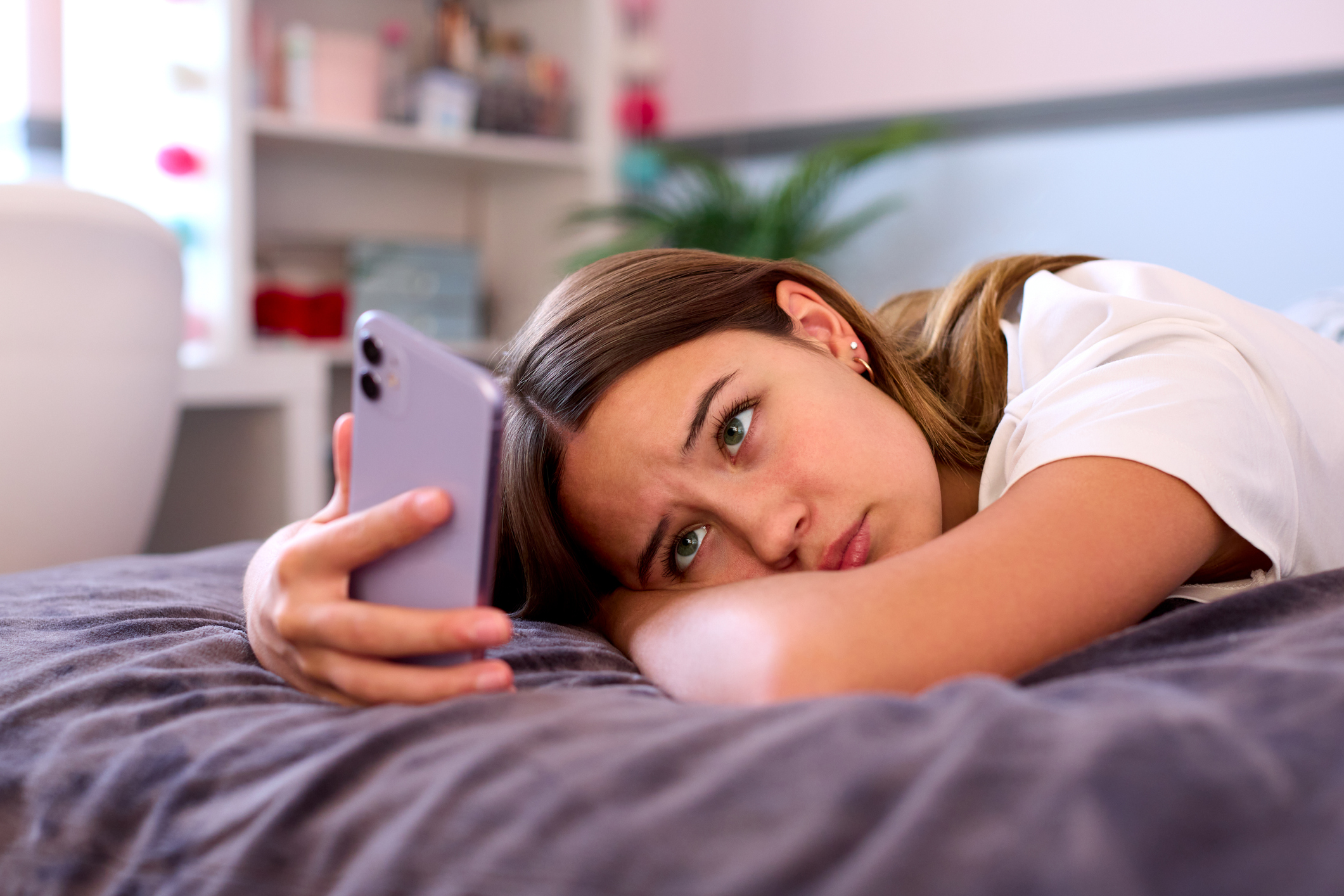 Depressed Teenage Girl Lying On Bed At Home Looking At Mobile Phone - kids in crisis