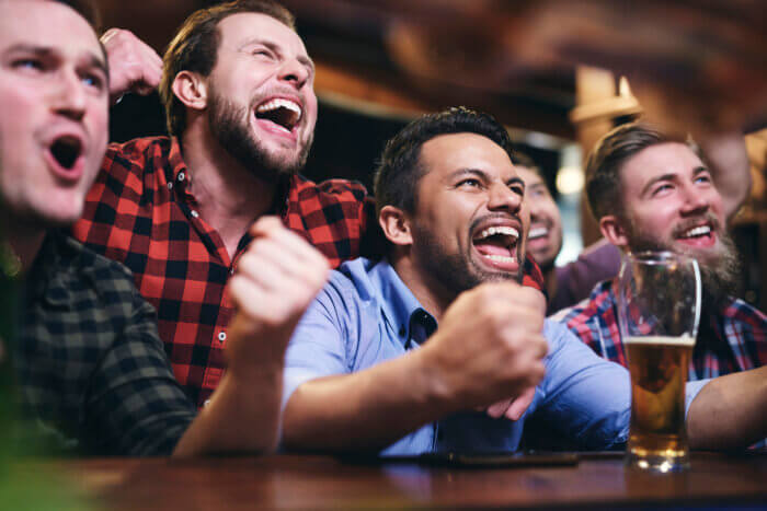 Men watching television and cheering for team at football bar for game day specials