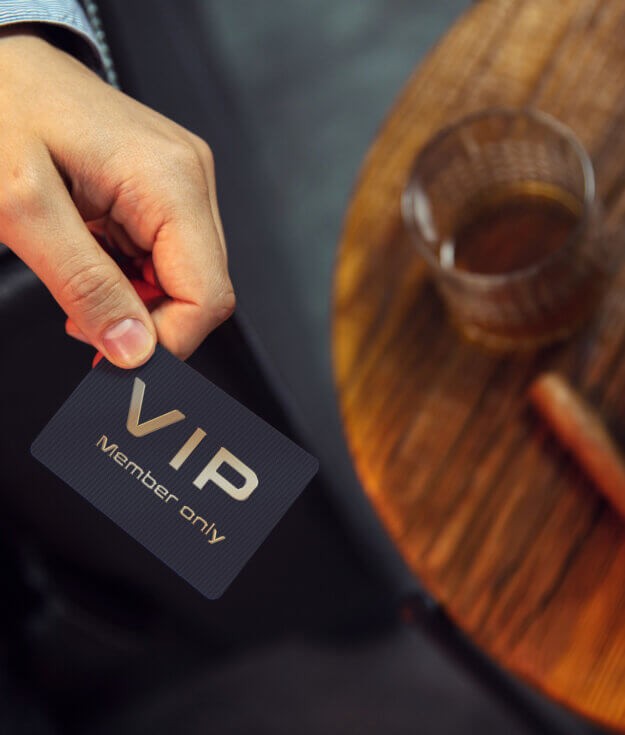 Man holds VIP member card. View from the top on the gentleman's hand that holds exclusive VIP membership card next to the wooden table with whisky in carafe and glass with cigars.