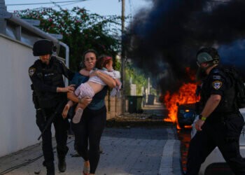 Police officers evacuate a woman and a child from a site hit by a rocket fired from the Gaza Strip, in Ashkelon, southern Israel, Saturday, Oct. 7, 2023. The rockets were fired as Hamas announced a new operation against Israel. (AP Photo/Tsafrir Abayov)