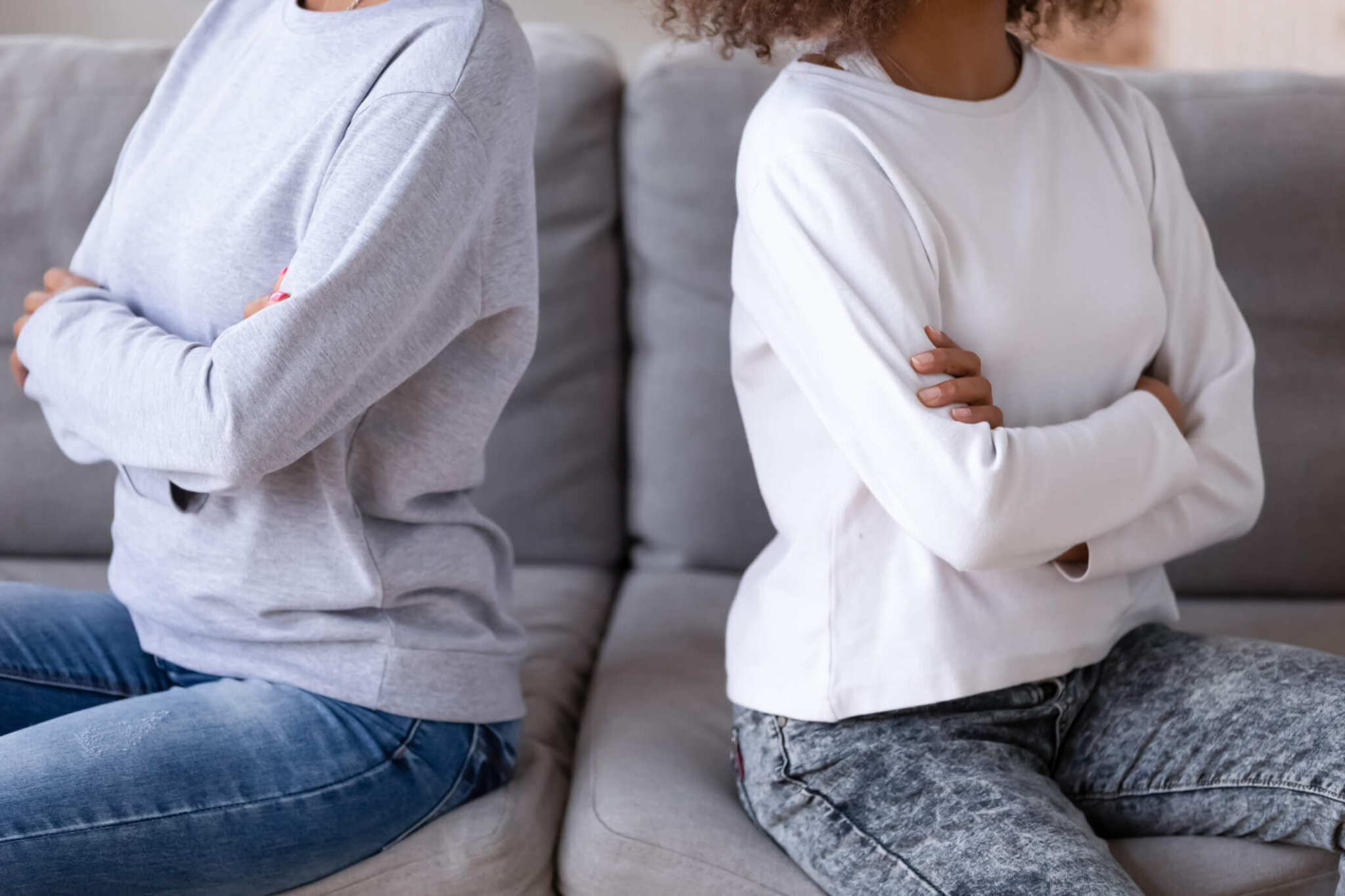 Close up African American mother and teen daughter after quarrel, sitting together on couch at home, ignore each other, stubborn mum and teenage child upset by agreement, family conflict concept (Getty Images)