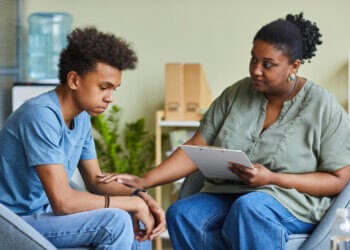 African psychologist supporting depressed teenage boy feeling guilty about behavior during therapy at office Mental Health