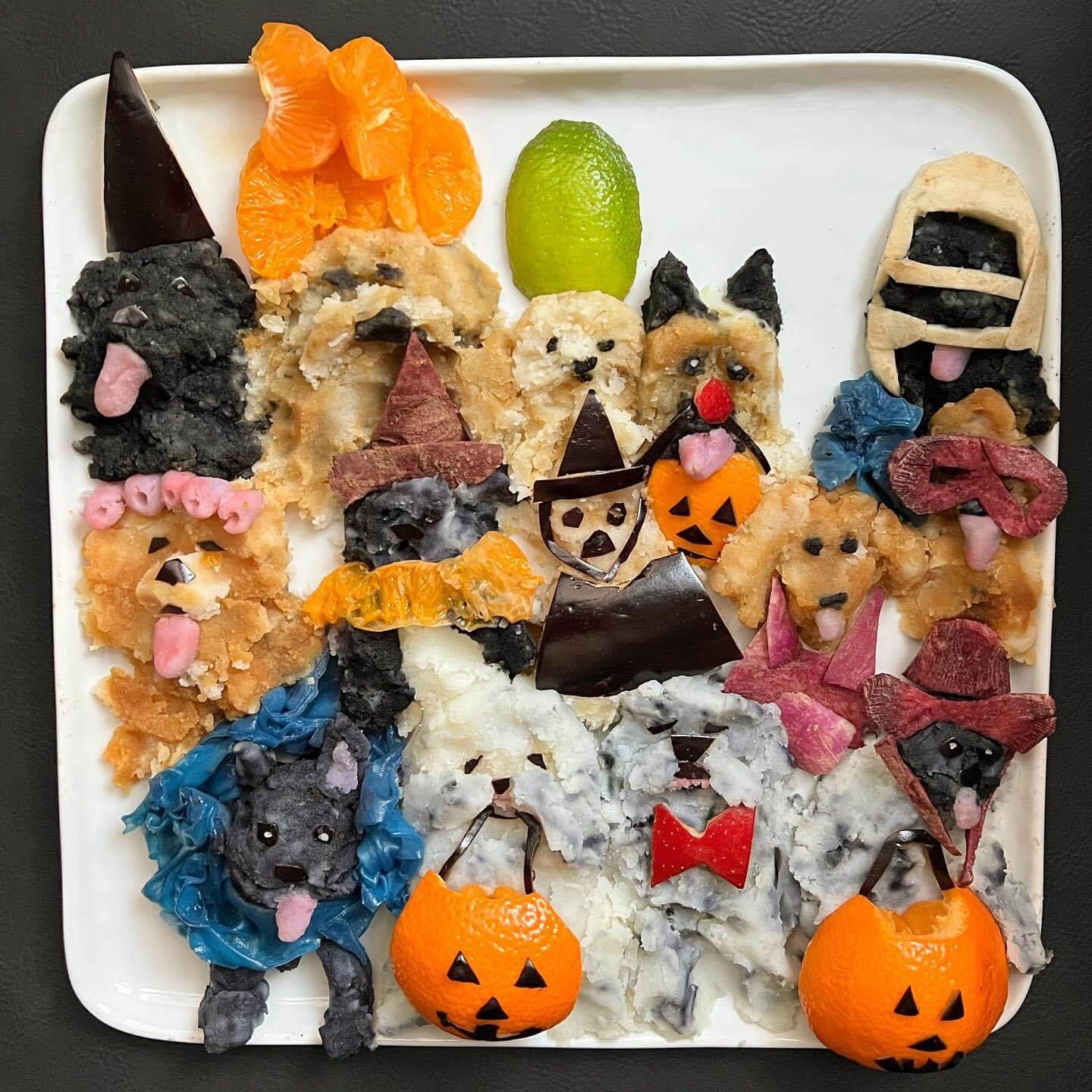 A pack of trick-or-treating dogs food art made from mashed potatoes, purple yams, clementines, eggplant, turnip, apple, rice paper, and lime, by Harley Langberg